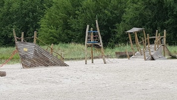 Ein sandiger Strand mit Holzspielgeräten, darunter eine Rutsche und eine Klettergerüst.
