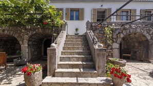 A stone staircase leading to a white building with wooden shutters, surrounded by stone arches and potted plants. - Unique mediterranean stone house with pool (Grižane)