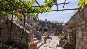 A stone courtyard with a rustic outdoor seating area, a stone oven, and a pergola with vines. - Unique mediterranean stone house with pool (Grižane)
