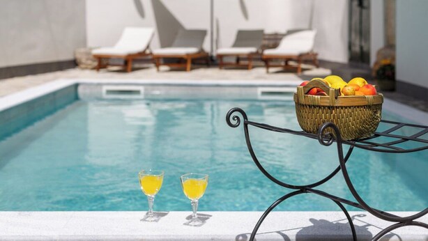 A poolside area with lounge chairs, a table with a fruit basket, and two glasses of a yellow beverage. - Unique mediterranean stone house with pool (Grižane)