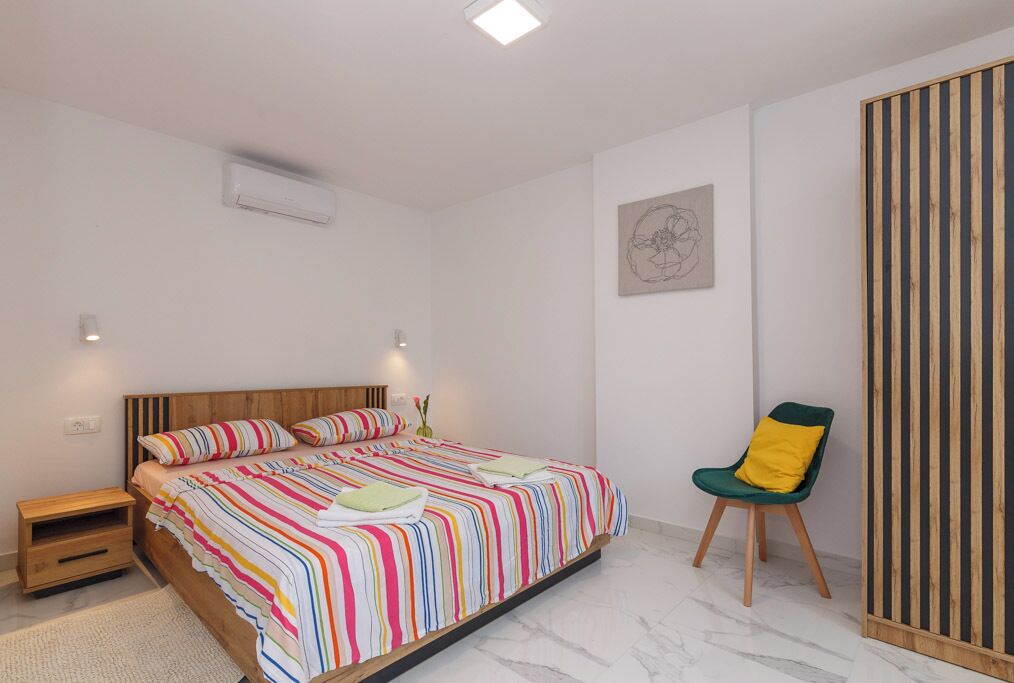 Een slaapkamer met een bed, nachtkastjes, een stoel en een wandairconditioner.