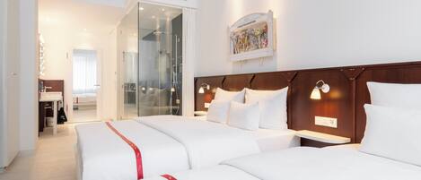 Habitación de hotel con dos camas, cabecero de madera, mesita de noche, espejo y mampara de ducha de vidrio.