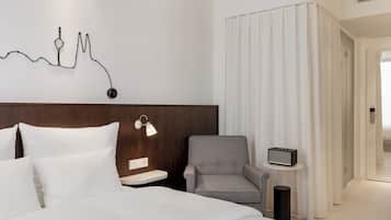 Una camera d'albergo con un letto, una poltrona grigia, un comodino con una lampada e un'opera d'arte a parete.
