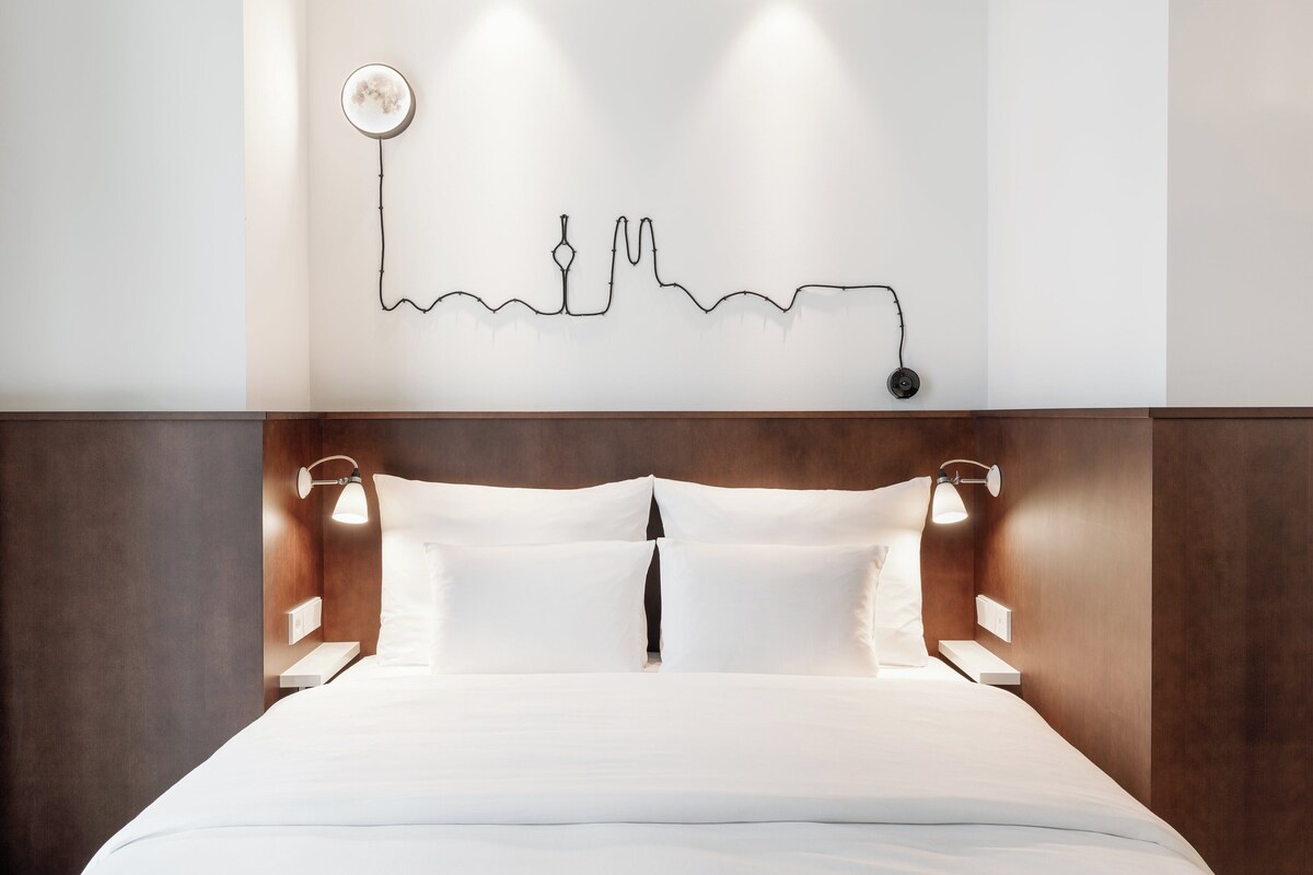 A neatly made bed with a headboard, two bedside lamps, and a wall-mounted artwork.
