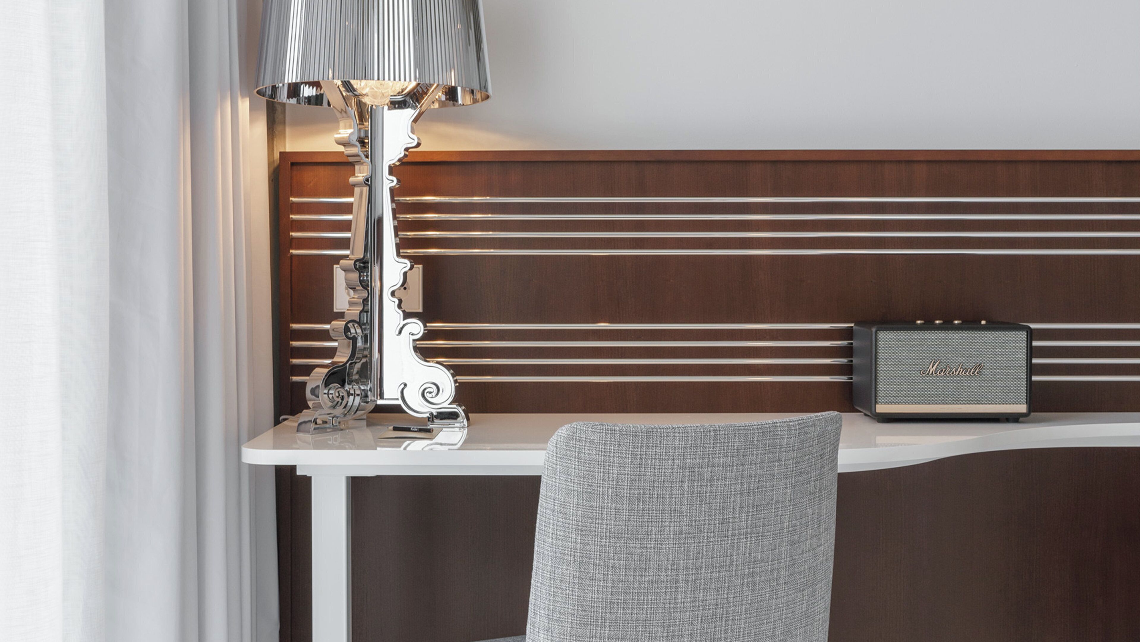 A hotel room with a white desk, a lamp, a radio, and a chair.