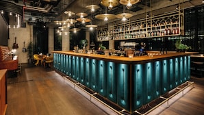 A bar area with a central bar, multiple hanging light fixtures, and a variety of bottles on shelves. - Ruby Ella Hotel Cologne by IHG (Cologne)