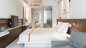 Une chambre d’hôtel moderne équipée d’un lit, d’une table de chevet, d’une télévision et d’une décoration murale représentant un paysage urbain.