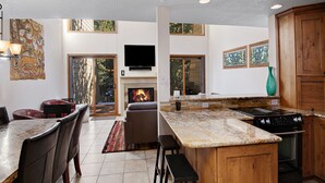 A modern kitchen with a large island, wooden cabinets, and a fireplace. - Casa Del Sol | 3BR+Loft Vail Townhome by Gore Creek, Pool (Vail)