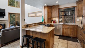 A modern kitchen with wooden cabinets, a granite countertop, and a built-in island with stools. - Casa Del Sol | 3BR+Loft Vail Townhome by Gore Creek, Pool (Vail)
