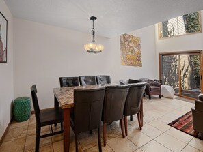 A dining area with a marble table and leather chairs, a hanging light fixture, and a large window with a view of trees.