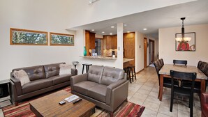 A spacious living room with a large brown leather sofa, a coffee table, and a dining area with a wooden table and chairs. - Casa Del Sol | 3BR+Loft Vail Townhome by Gore Creek, Pool (Vail)