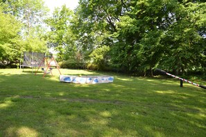 A grassy outdoor area with a swing set, a small pool with a cloud pattern, and a rope barrier. - Seemann, Thorsten 1 - Seemann, Thorsten (Insel Poel)