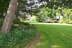 Une zone verdoyante bien entretenue, avec un petit bâtiment, entourée d’arbres et d’arbustes.