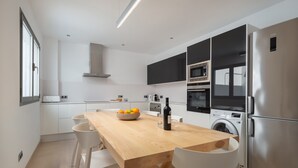 Eine moderne Küche mit einem Holzespeisetisch, weißen Stühlen, einer Waschmaschine und einem Edelstahlkühlschrank.