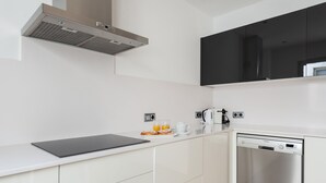 Eine moderne Küche mit weißen Schränken, einer schwarzen Arbeitsplatte, einem Edelstahl-Geschirrspüler und einem schwarzen, an der Wand montierten Fernseher.