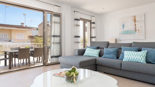 Ein modernes Wohnzimmer mit grauem Sofa, einem Glastisch und einem Balkon mit Gartenmöbeln.