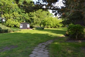 A small wooden cabin surrounded by lush greenery and a stone pathway leading to it.