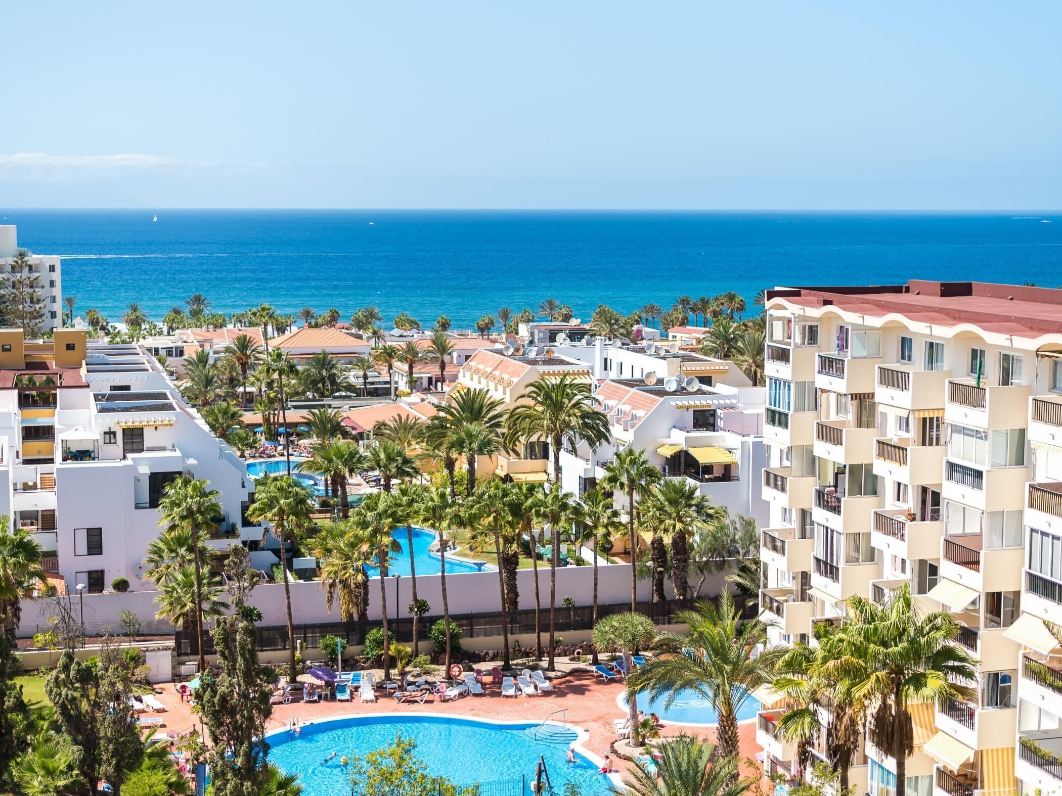 A resort with multiple swimming pools surrounded by palm trees and a view of the ocean.