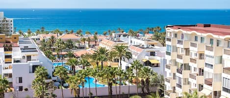 Un resort con varias piscinas rodeadas de palmeras y vista al océano.