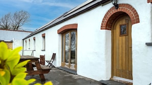 A white building with a wooden door and arched windows, a wooden bench, and a clear sky. - Orchard Cottage - Luxury Barn Conversion (Tenby)