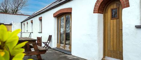 A white building with a wooden door and arched windows, a wooden bench, and a clear sky.