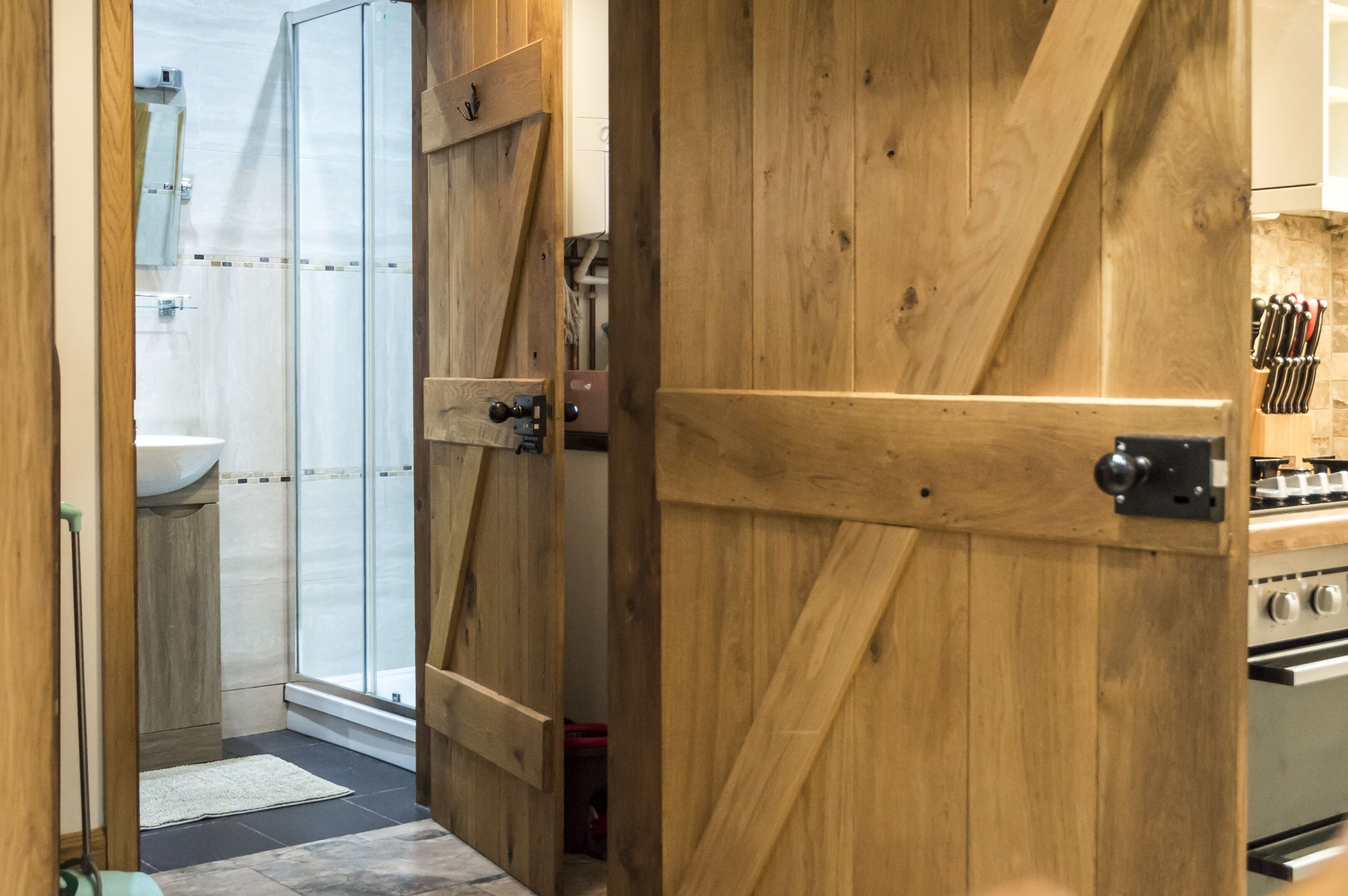 A wooden door leading to a bathroom with a shower and a sink.
