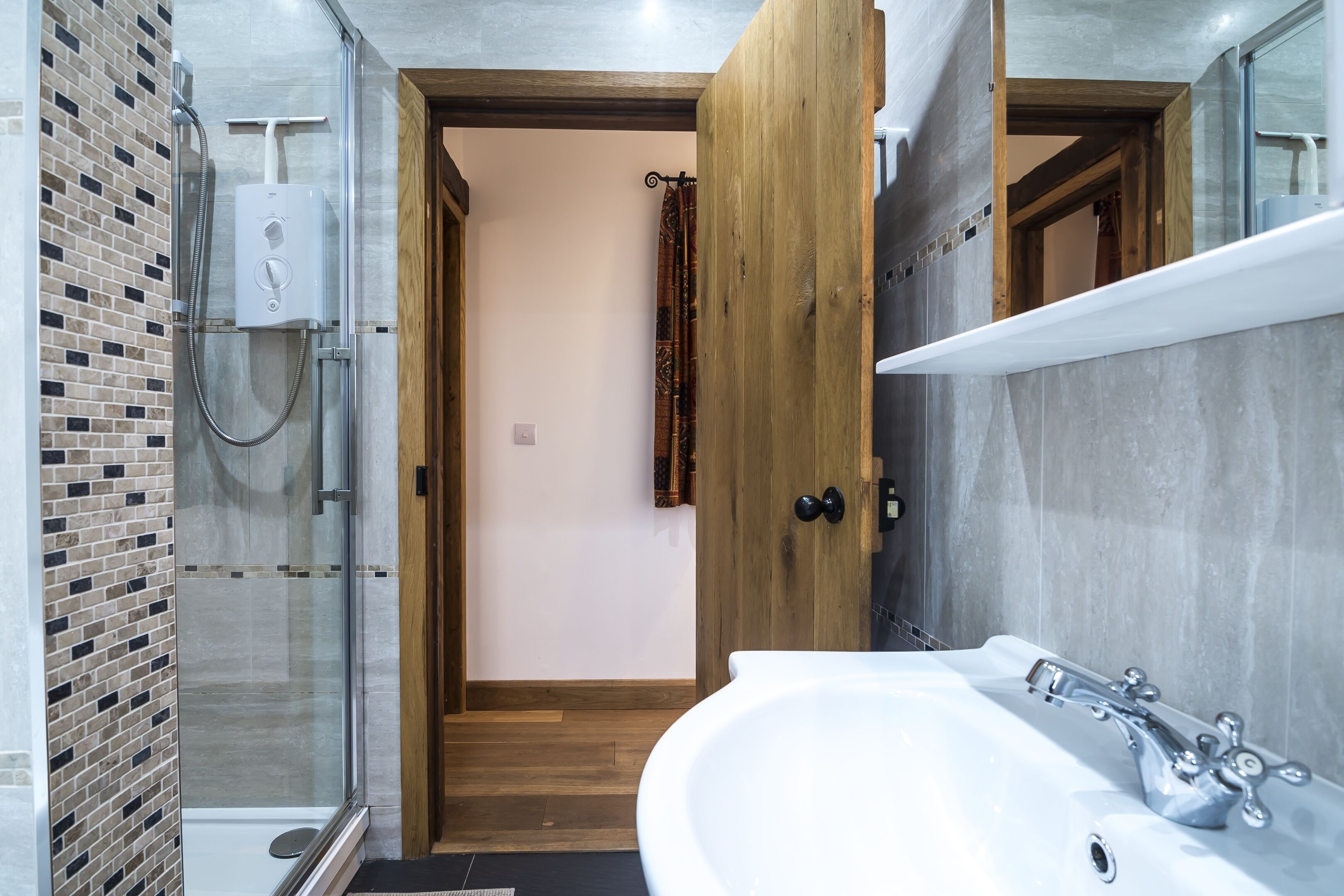 A modern bathroom with a glass-enclosed shower, a white sink, and a wooden door leading to another room.