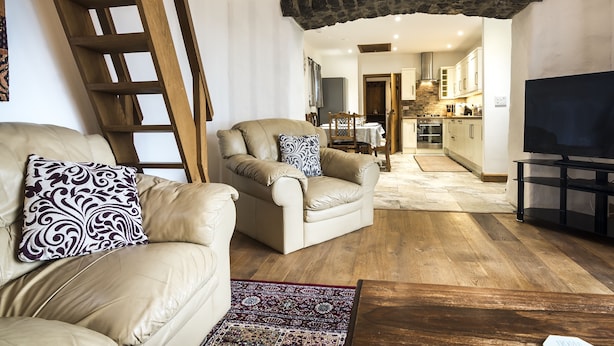 A living room with a leather sofa, a wooden coffee table, a patterned rug, and a television on a stand. - Orchard Cottage - Luxury Barn Conversion (Tenby)