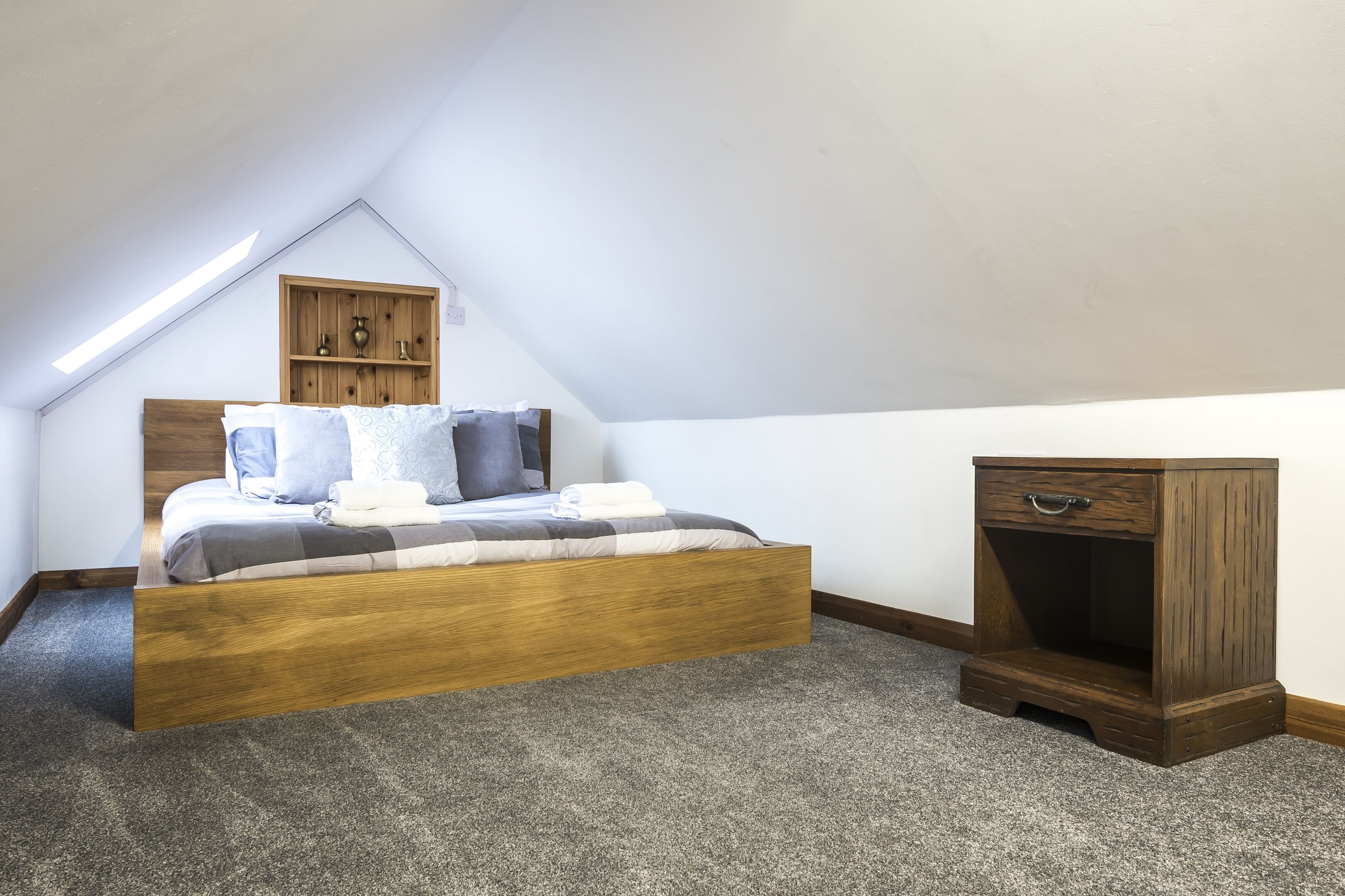 A bedroom with a sloped ceiling, a bed with a wooden headboard, a bedside table, and a nightstand.