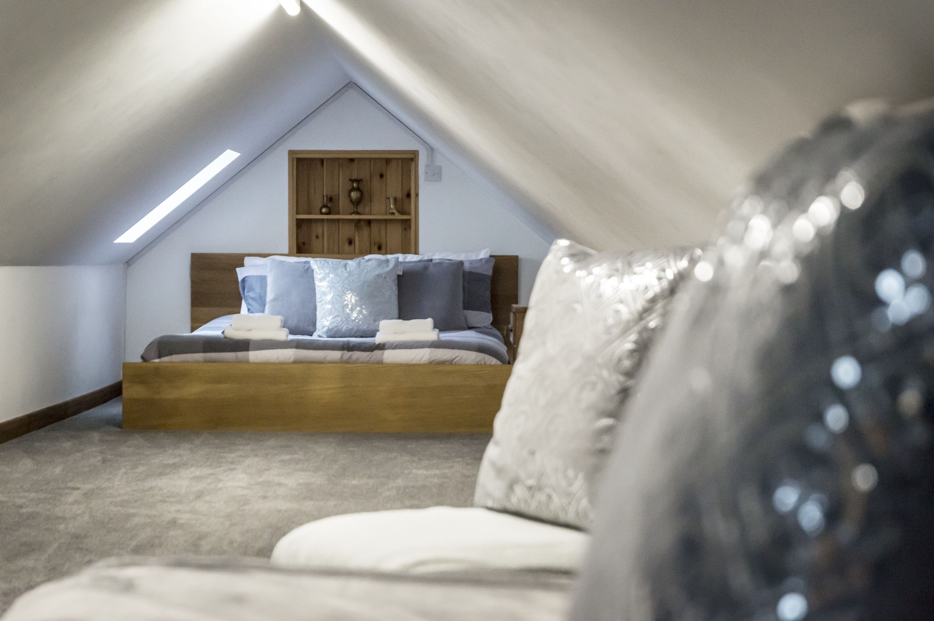 A bedroom with a sloped ceiling, a wooden headboard, a bed with blue and white bedding, and a wooden shelf above the bed.