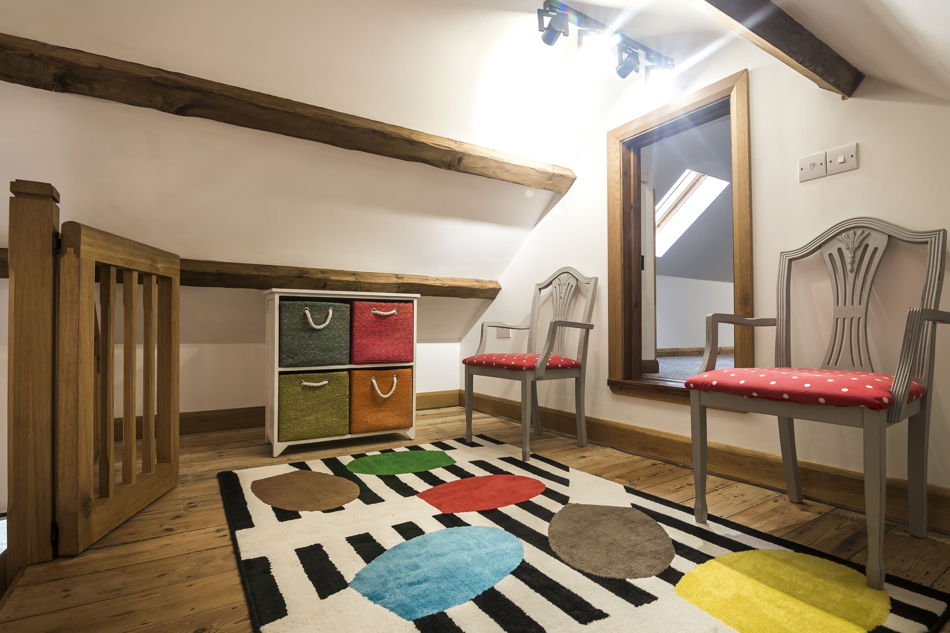 A loft bedroom with exposed wooden beams, a loft bed, a colorful rug, and a chest of drawers with storage bins.