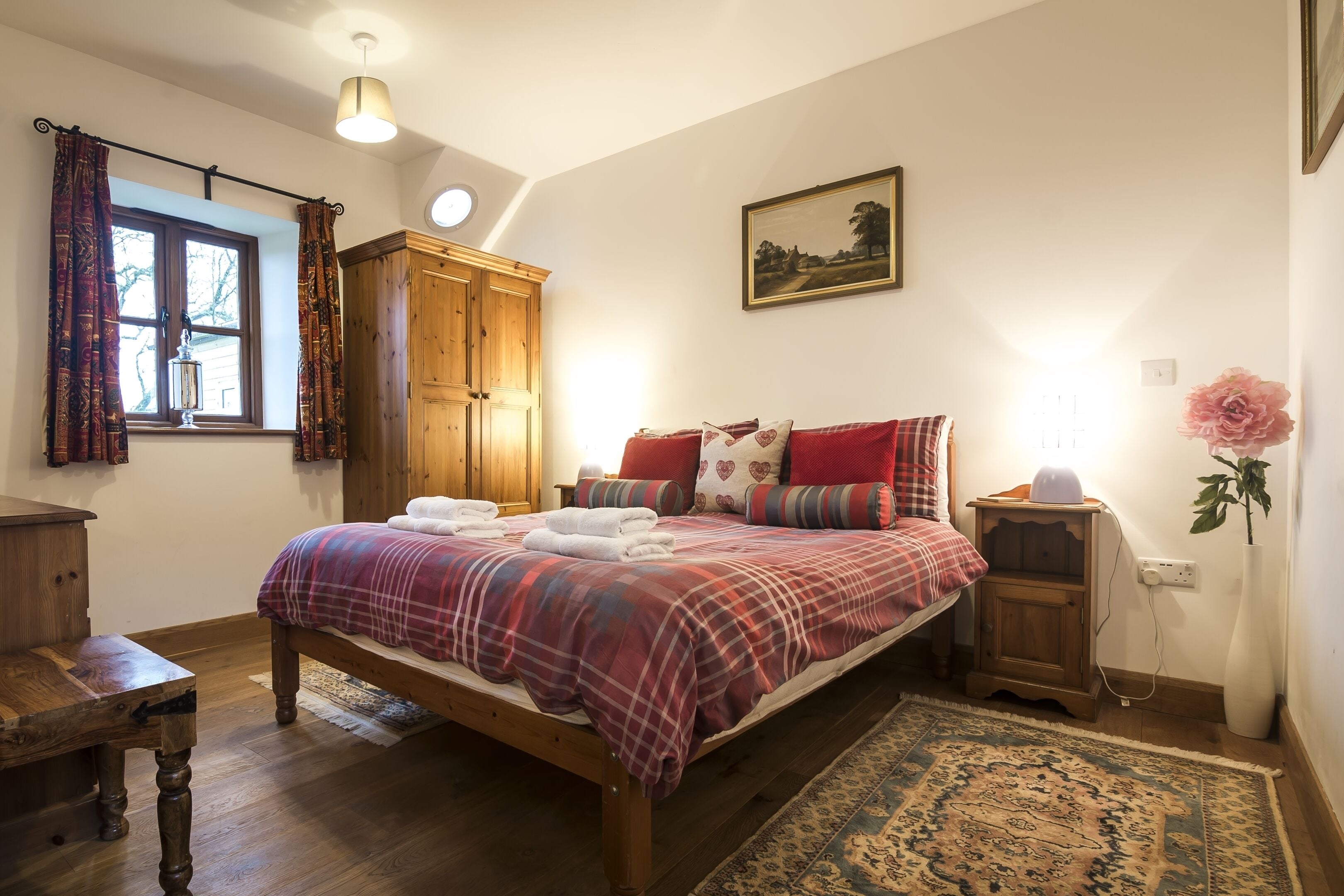 A bedroom with a wooden bed, a nightstand, a wardrobe, a window with curtains, a painting on the wall, and a rug on the floor.