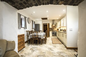 Un comedor con suelo de piedra, mobiliario de madera y una cocina al fondo.