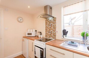 A compact kitchen with a microwave, kettle, and a glass stovetop.