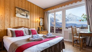 Un dormitorio con paneles de madera, una cama grande, un escritorio de madera y vista a una montaña.