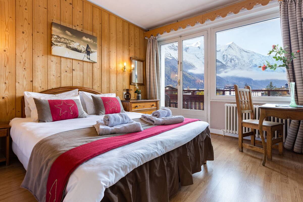 Un dormitorio con paneles de madera, una cama grande, un escritorio de madera y vista a una montaña.