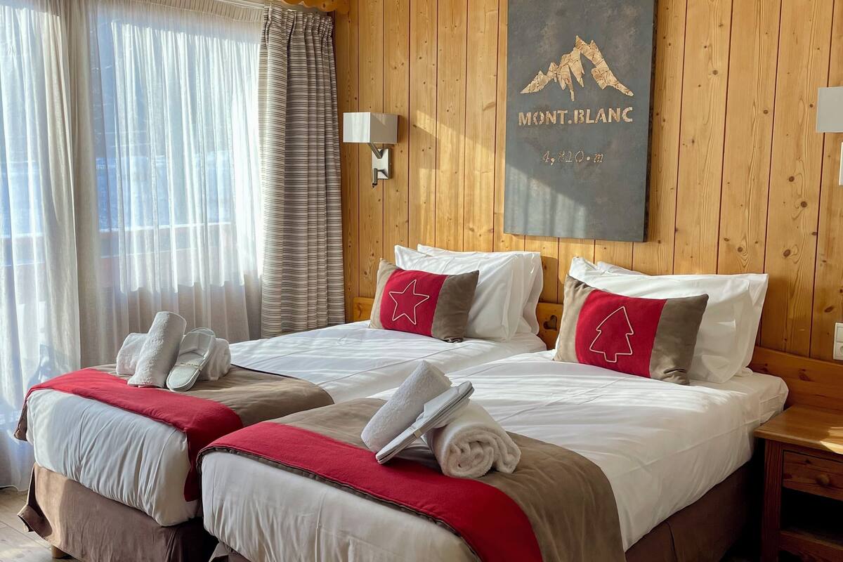 Habitación de hotel con dos camas, paneles de madera en las paredes, una obra de arte con temática de montaña y un ventanal con cortinas.