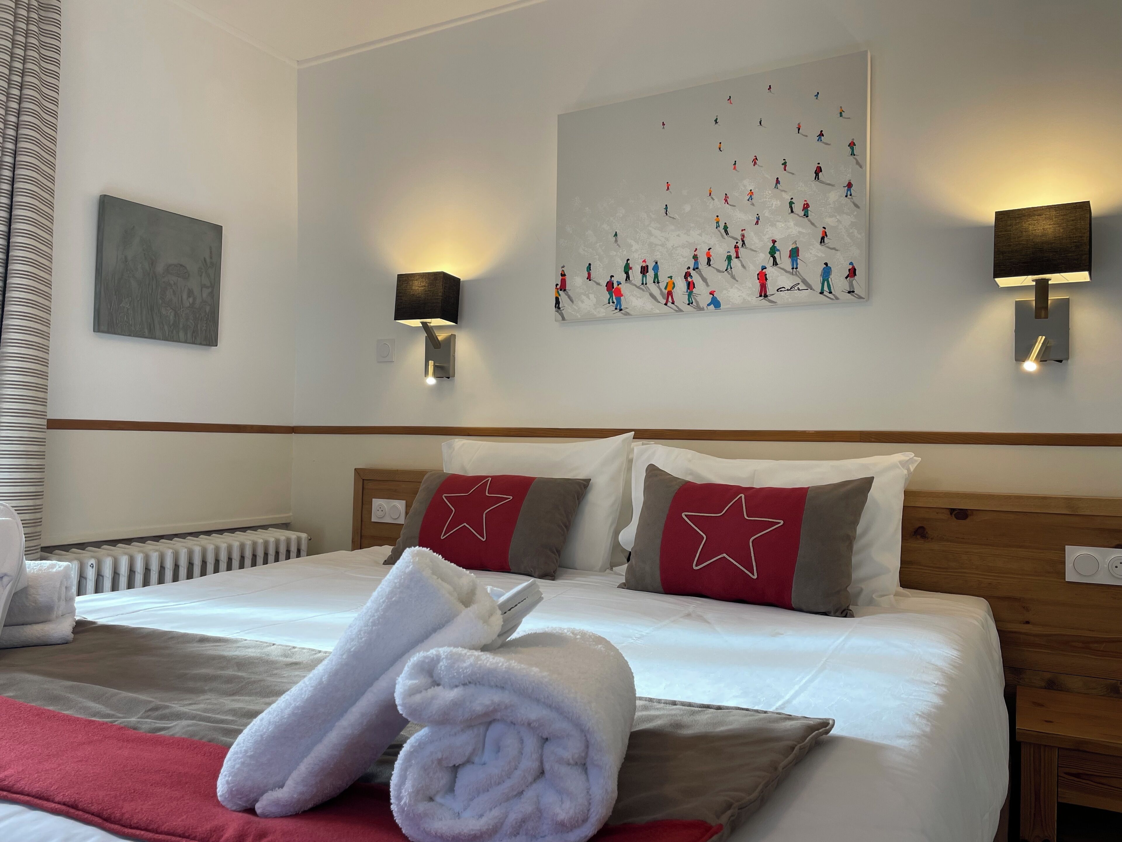 A hotel room with a neatly made bed, a large painting on the wall, and two wall-mounted lamps.