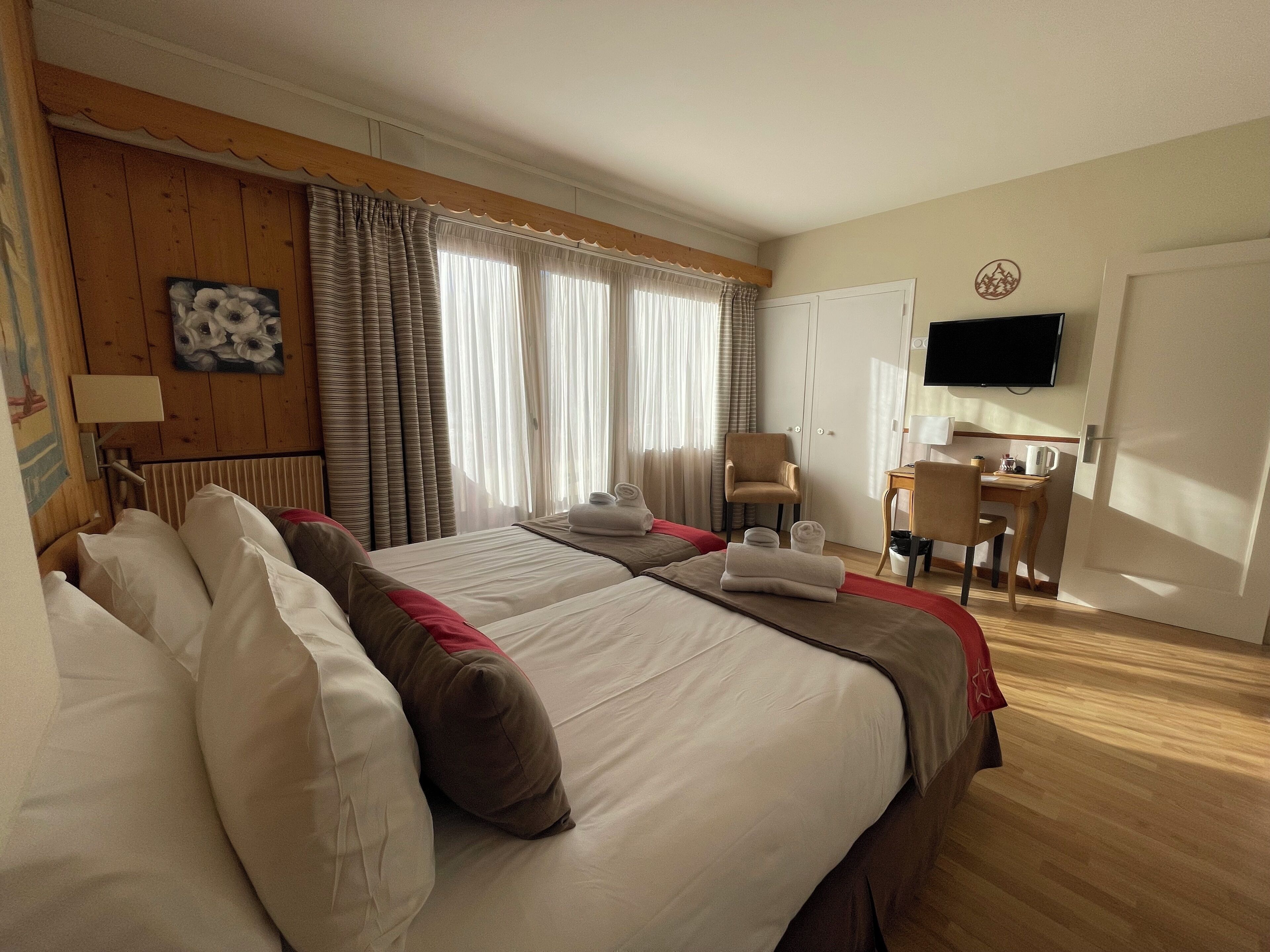 Hotellihuone, jossa on kaksi sänkyä, työpöytä, tuoli, televisio ja ikkuna, jossa on verhot.