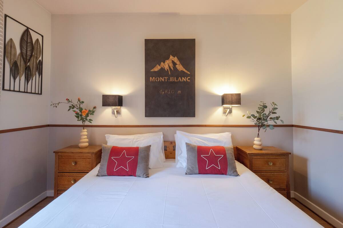 Una habitación de hotel con una cama grande, dos mesitas de noche con lámparas, un cuadro enmarcado en la pared y un jarrón decorativo en la mesita de noche.