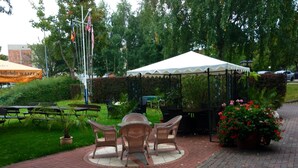 An outdoor patio area with wicker furniture, a white canopy, and potted plants. - Hotel Bertramshof (Wismar)