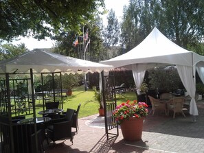 A covered outdoor seating area with tables and chairs, surrounded by greenery and trees. - Hotel Bertramshof (Wismar)