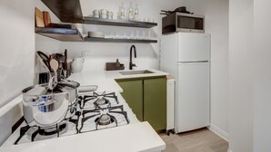 Una cocina compacta con estufa a gas, armarios blancos, microondas y refrigerador.