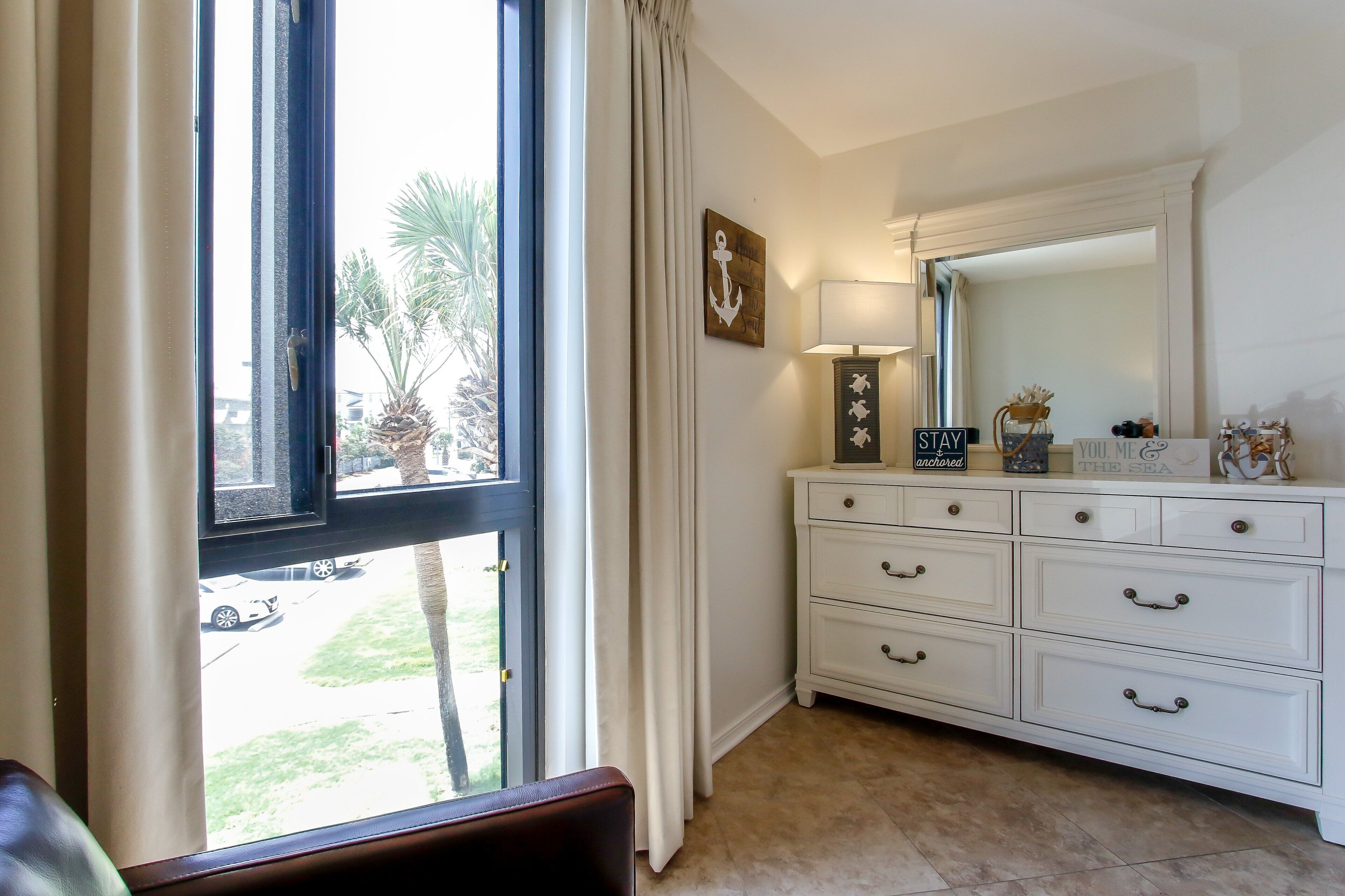 A room with a white dresser, a mirror, and a window with curtains.