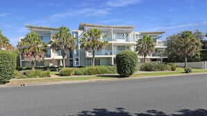 A modern multi-story hotel with balconies, palm trees, and well-maintained landscaping. - Beachfront on Bennetts | Beaches Apartment 4 (Hawks Nest)