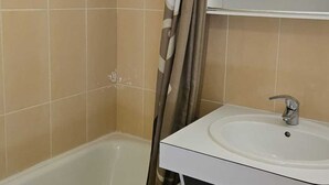 Ett badrum med beige kakel, en vit handfat med ett silverfärgat blandare och en duschdraperi.