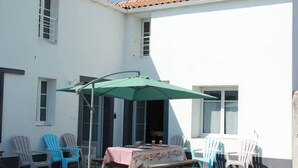 Un espace patio avec une table et des chaises, un parasol vert et un bâtiment blanc doté de fenêtres.