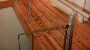 Un escalier en bois avec des rampes en métal mène à une pièce dotée d’une porte blanche et d’un mur d’accent rouge.