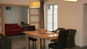Un coin repas avec une table et des chaises en bois, un canapé rouge et une grande fenêtre avec des stores.
