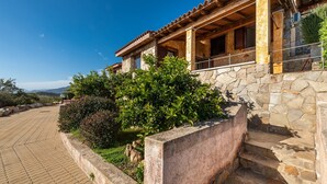 A stone house with a tiled roof, a stone staircase, and a paved area with greenery.